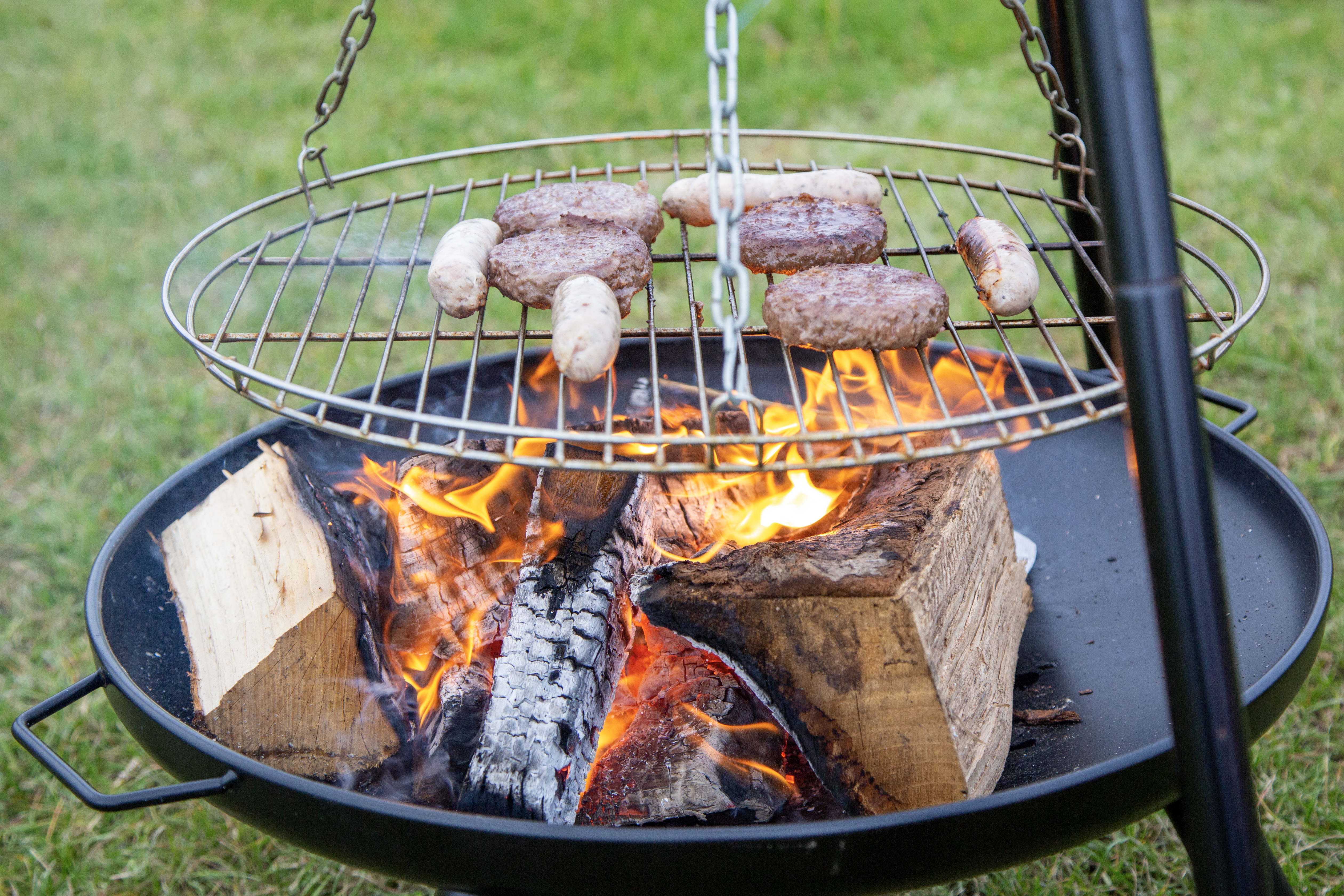A fire pit with some burgers and sausages cooking on a grill.